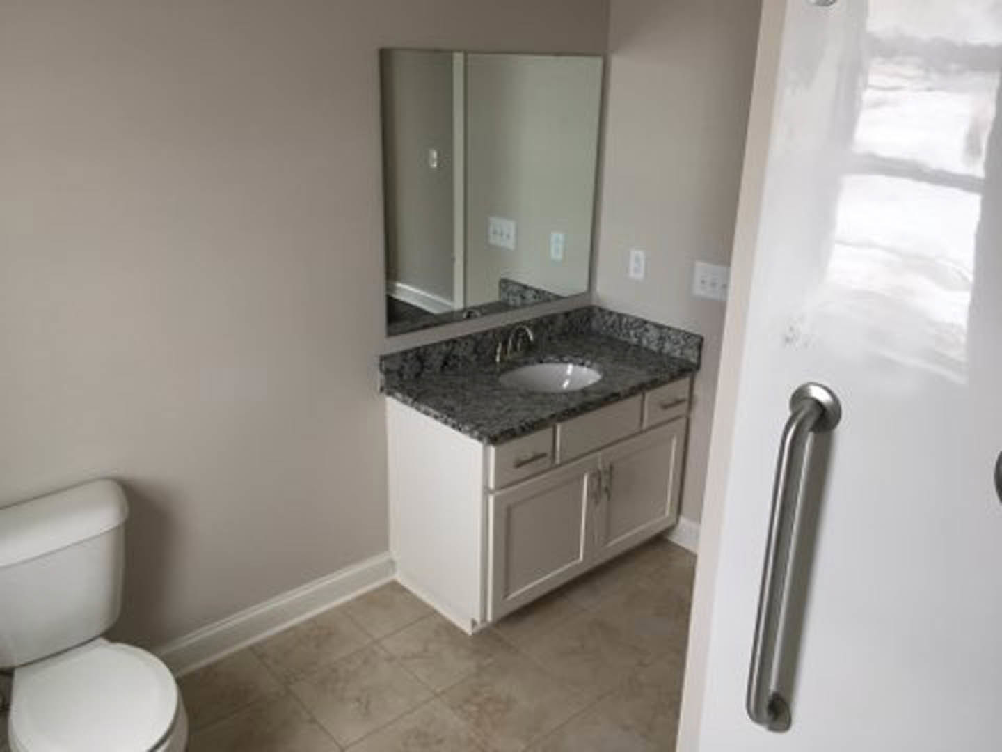Modern bathroom featuring a white porcelain sink with chrome faucet, matching toilet, light gray tile flooring, white cabinetry, and a large wall mirror above the countertop