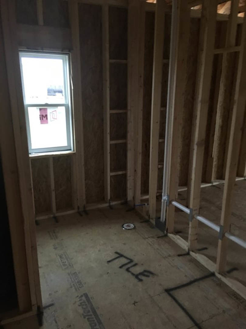Wood-framed room with exposed studs, concrete floor, large window featuring a pink sign, and visible building insulation