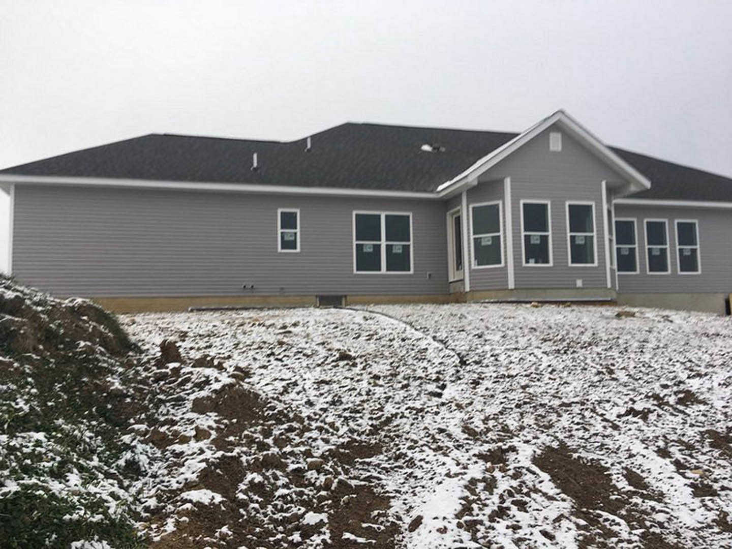 Two-story house with black roof, white-framed windows, and light siding, surrounded by snow-covered ground under a winter sky