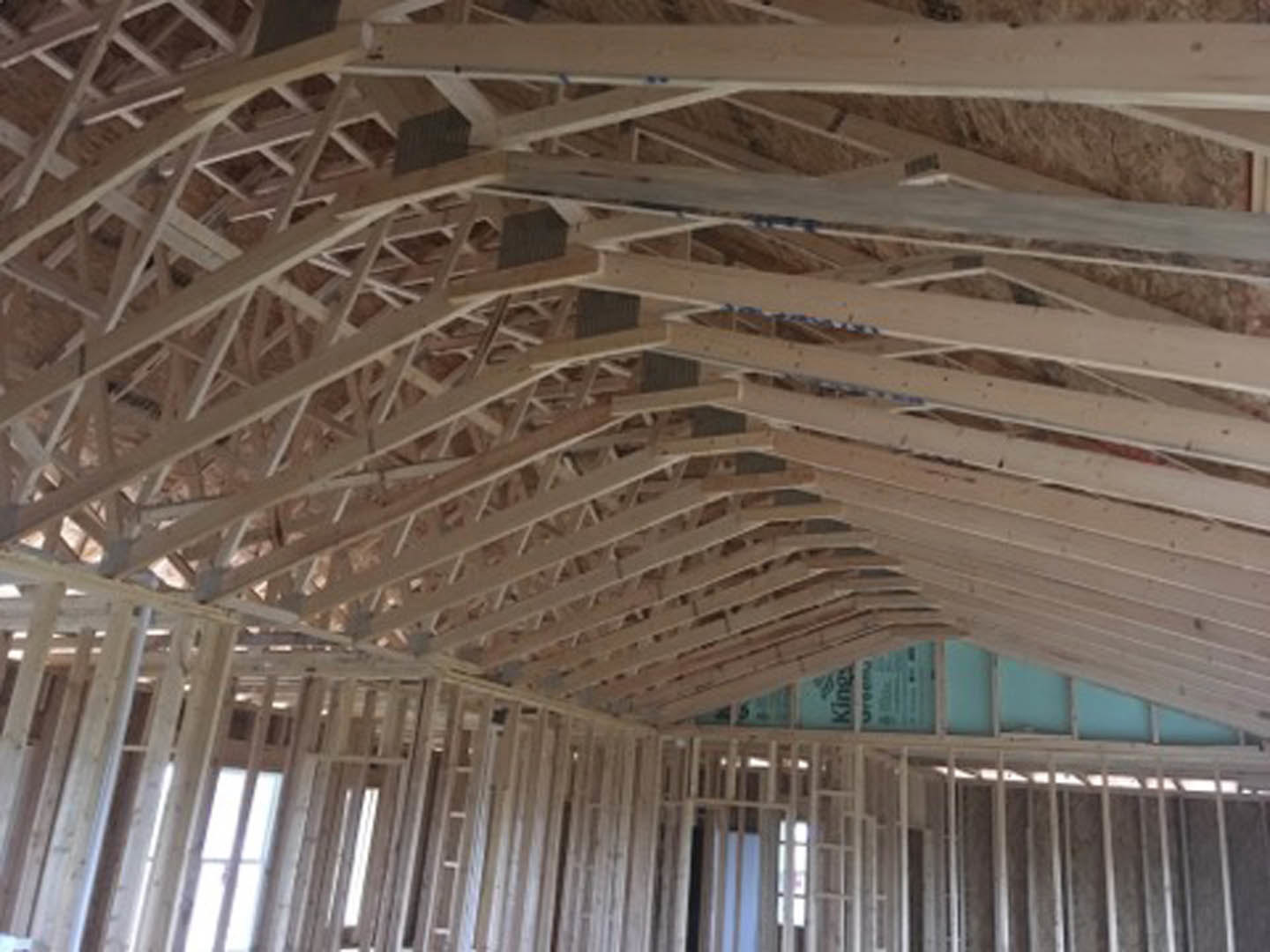 Exposed wood framing and beams inside a partially constructed house, natural daylight filtering through open window spaces