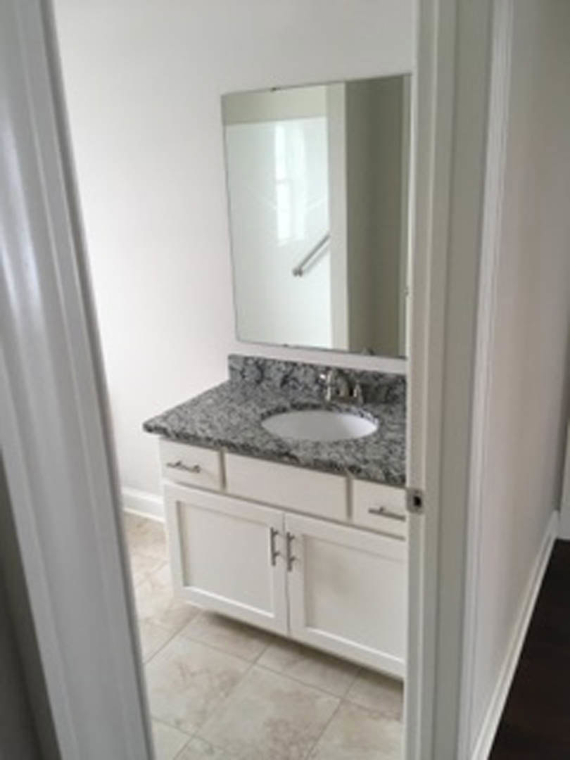 Bathroom with granite countertop, white undermount sink, tile backsplash, large framed mirror, and white cabinetry.