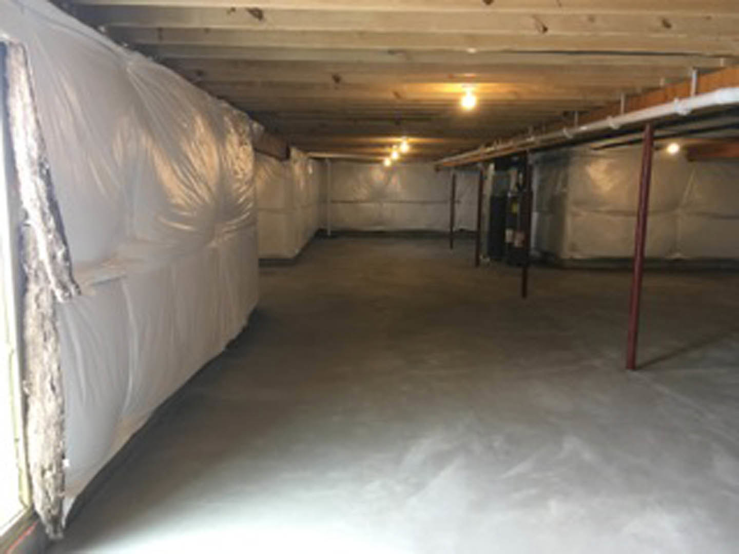 Basement with white bags stacked on the floor, white couch draped with a white blanket, white walls and curtain, light-colored ceiling, and a blurry dog in the foreground.