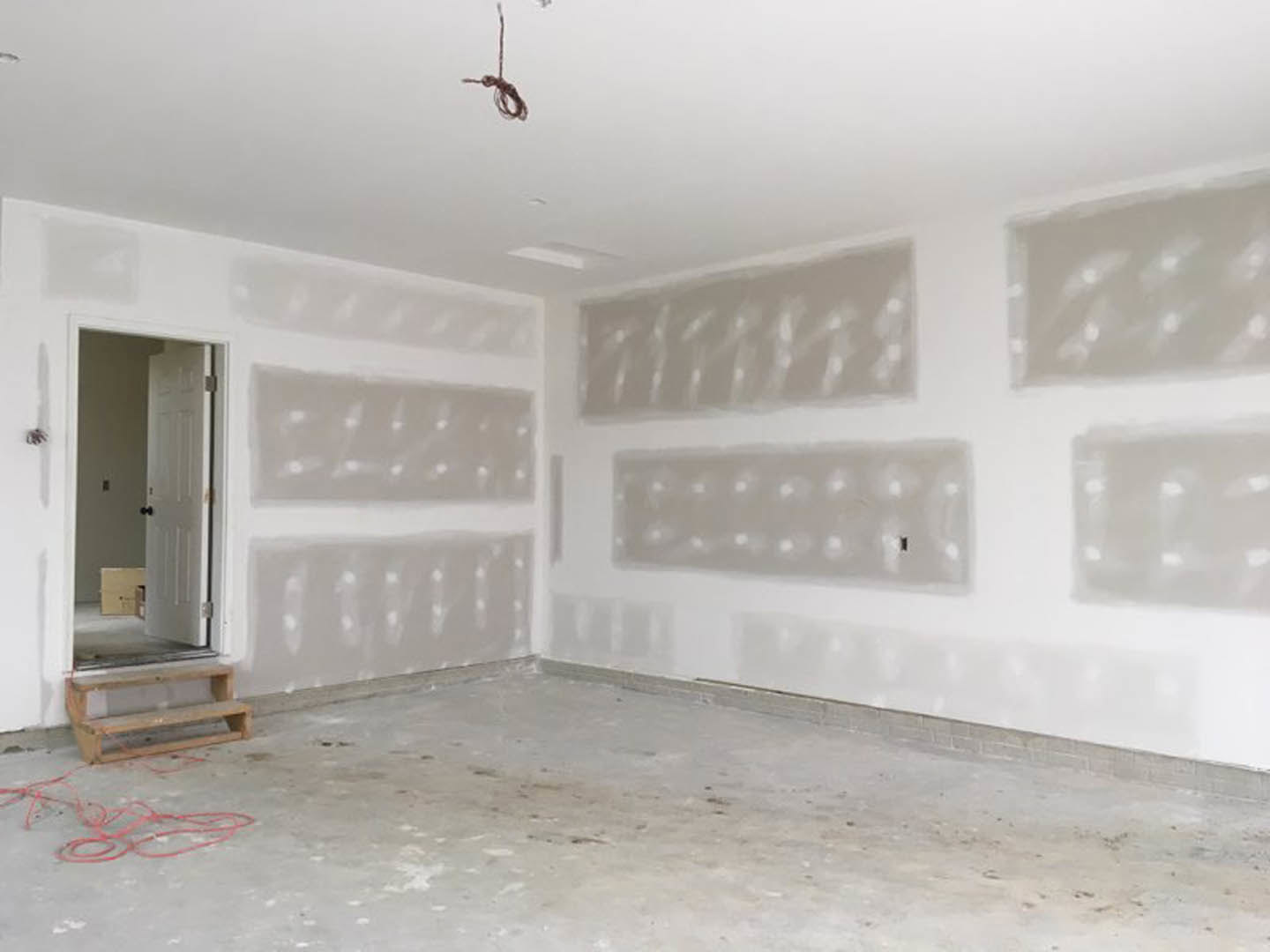 White-walled room with a white door featuring black knobs, tile flooring, wooden step stool, red wire on the ground, and concrete floor detail.