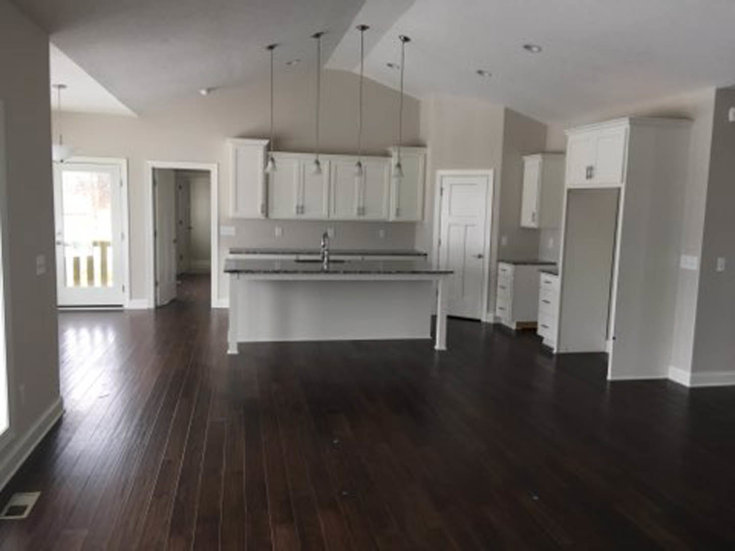 Spacious kitchen featuring a large central island with white quartz countertop, dark wood flooring, white cabinetry, tile backsplash, and stainless steel appliances.