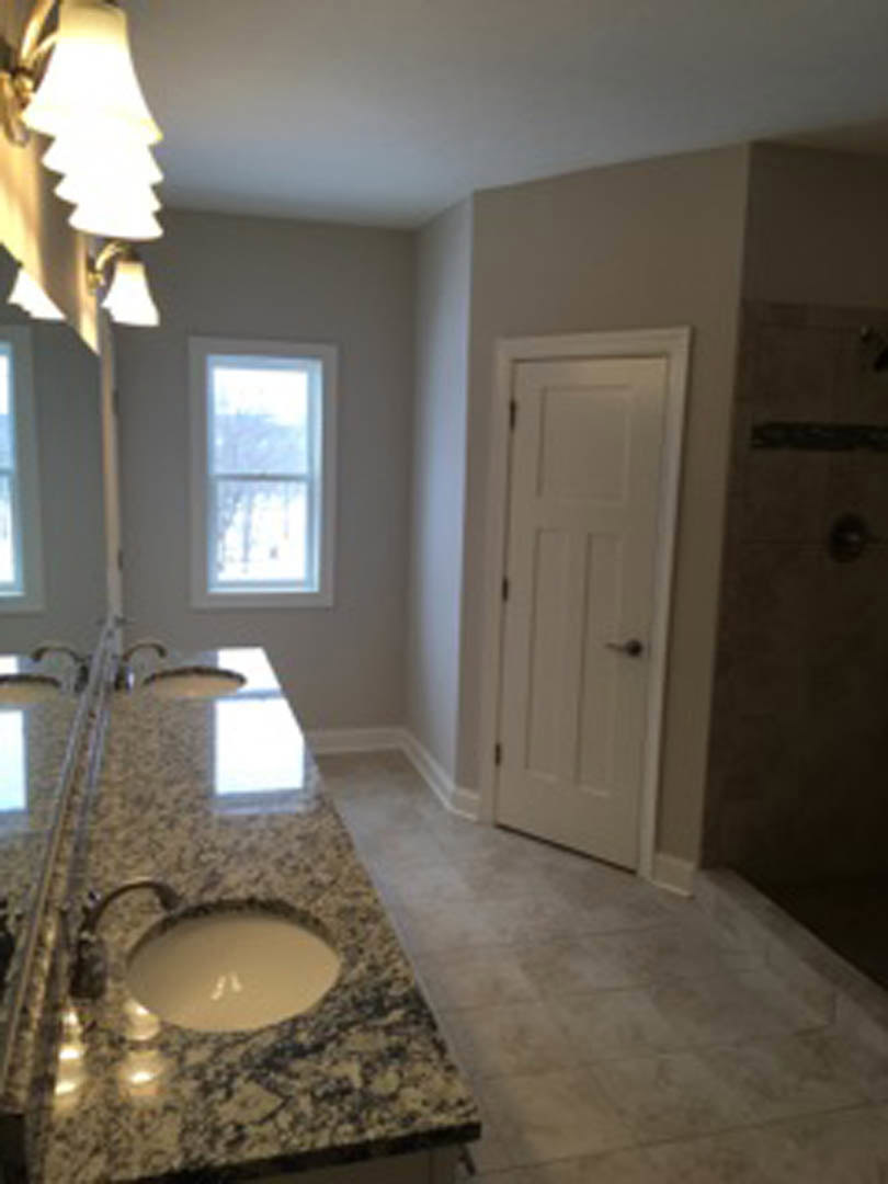 Modern bathroom with dual sinks, chrome faucets, white countertop, large wall mirror, white paneled door with black handle, window with white trim, and ceiling lamp.