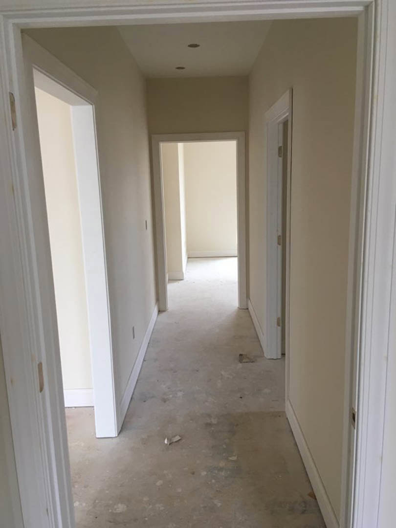 Hallway with smooth white walls, white trim, white door with matching frame, black baseboard, light-colored flooring, and recessed ceiling lighting