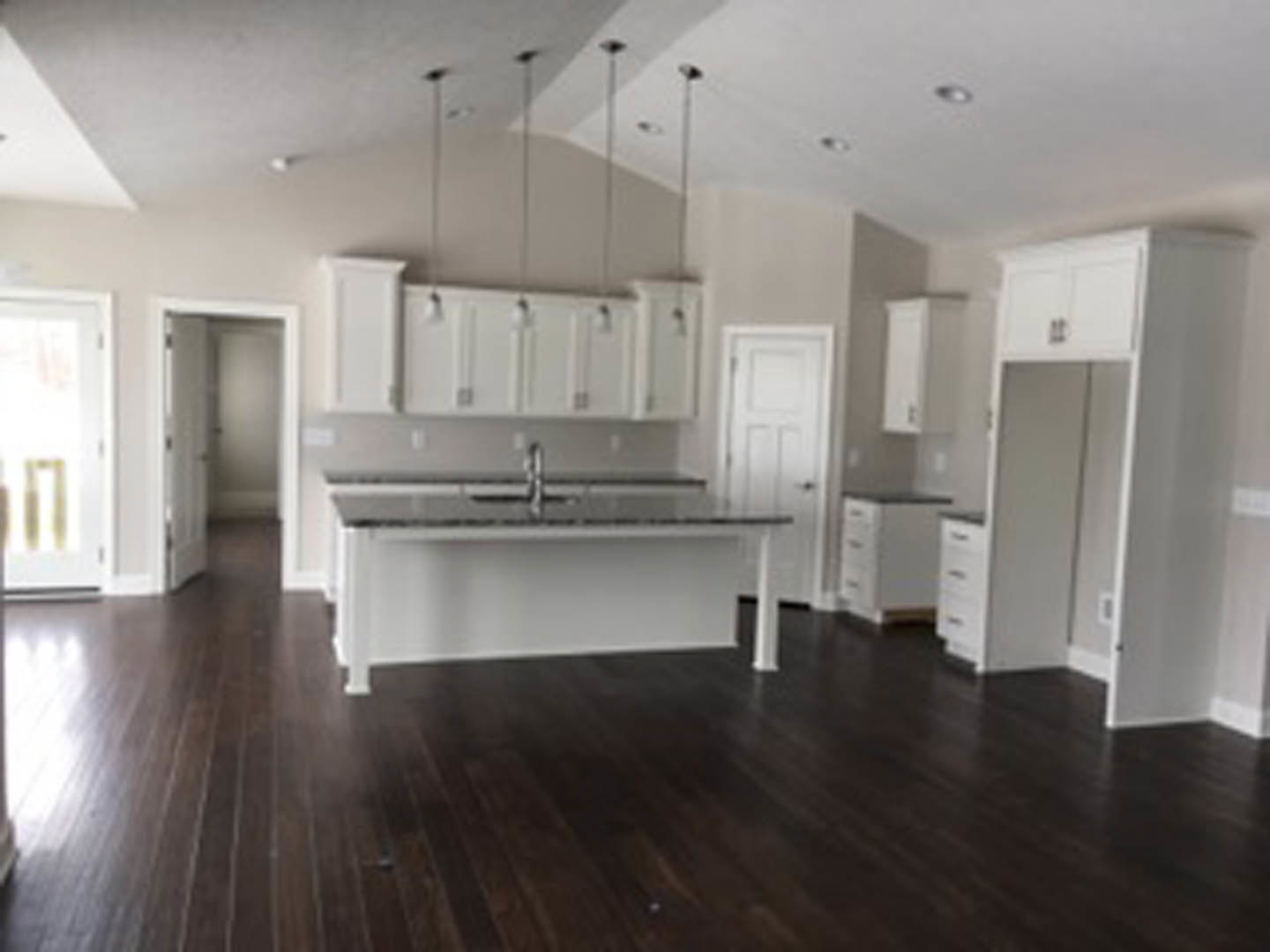 Spacious kitchen featuring a large central island with a built-in sink, dark wood flooring, white cabinetry, and light-colored tile backsplash.