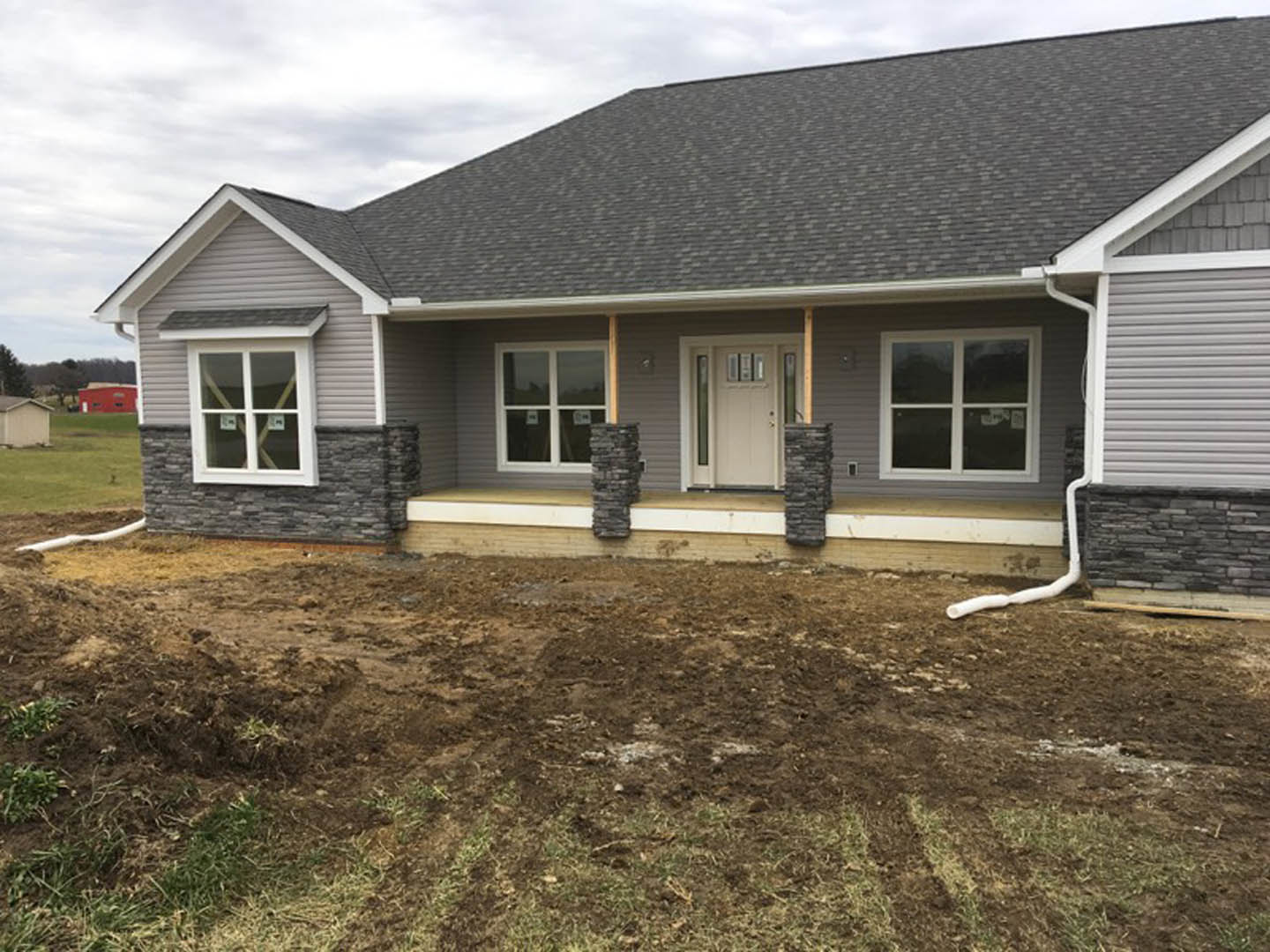 Two-story white house under construction with exposed dirt patches in front yard, white framed windows, and covered porch.