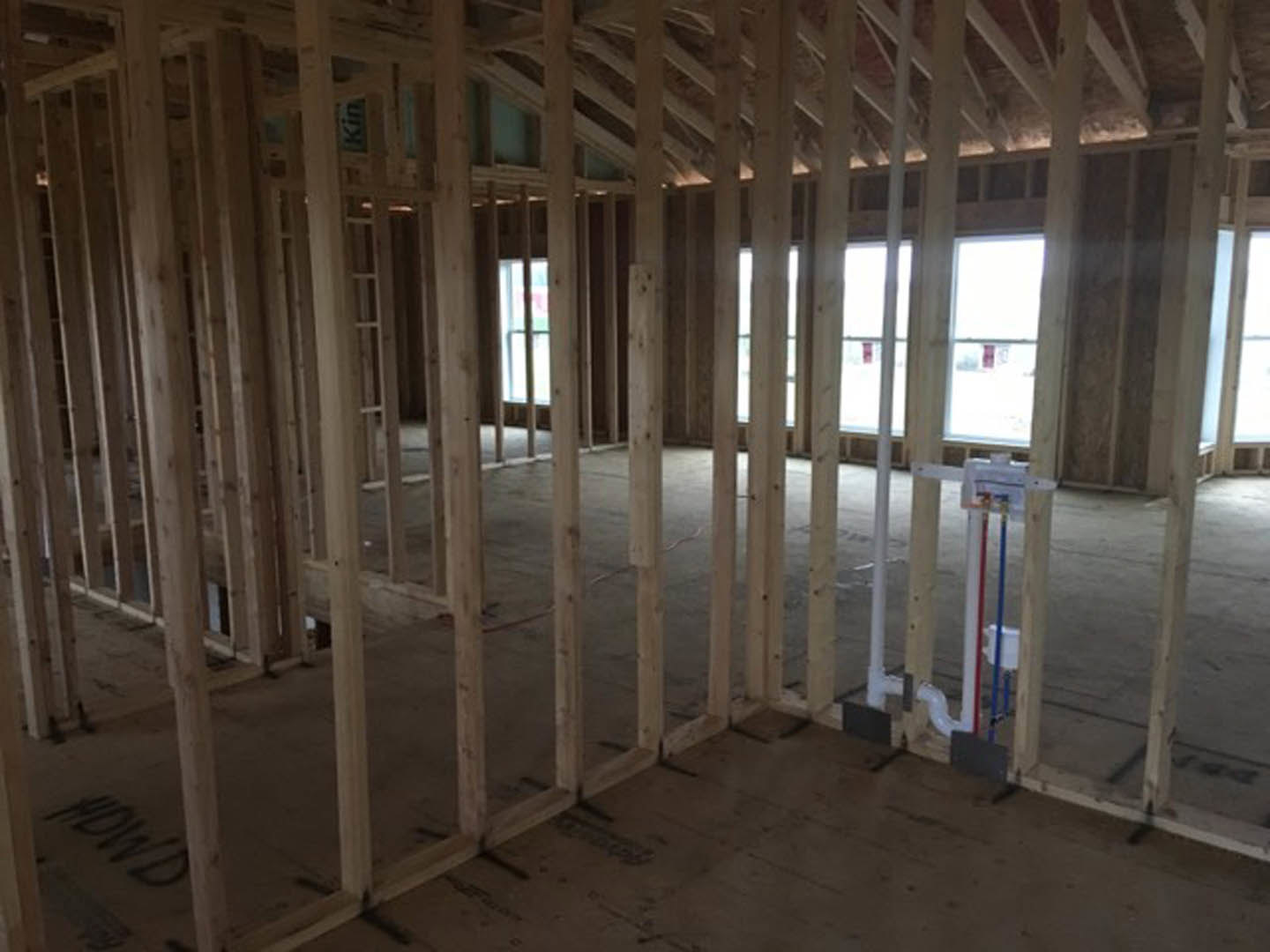 Room under construction with exposed wood framing, ceiling beams, and large windows letting in daylight