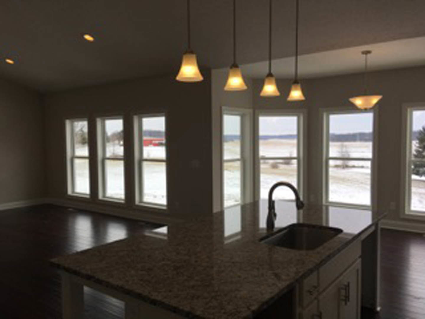 Spacious kitchen featuring a large central island with stone countertop, white cabinetry, stainless steel sink, pendant lights overhead, and expansive windows providing natural