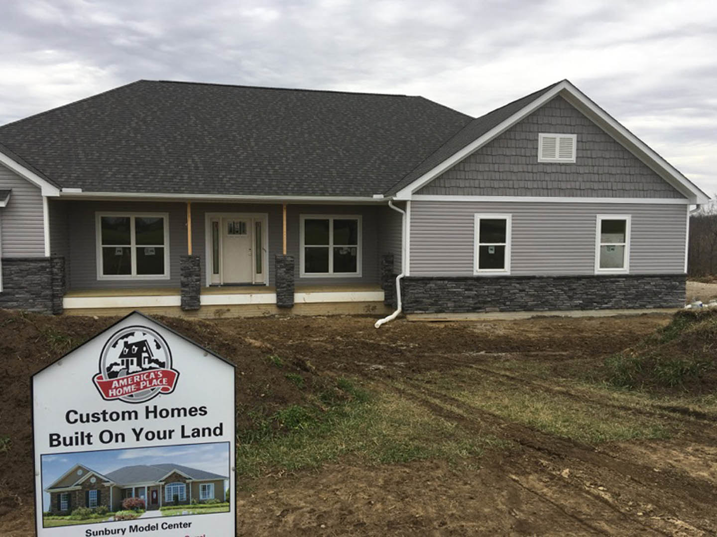 Partially finished house with light siding, white framed windows, glass-paneled white door, wall vent, and construction sign in front.
