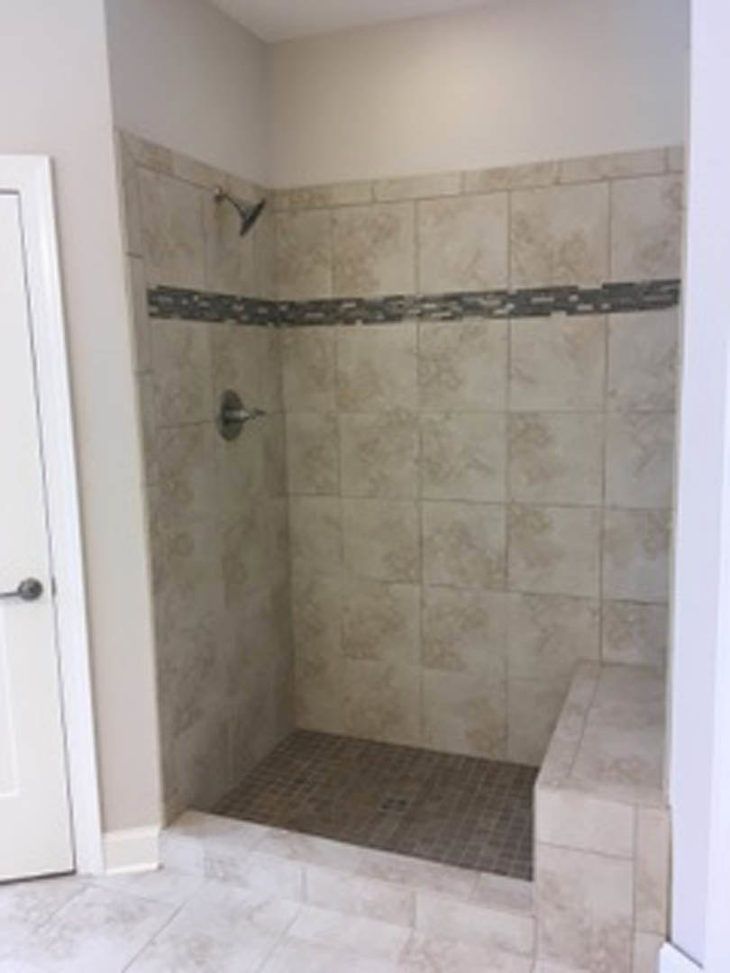 Walk-in shower featuring square marble tile floor, white tile walls, and a white plaster wall with a visible crack in the corner