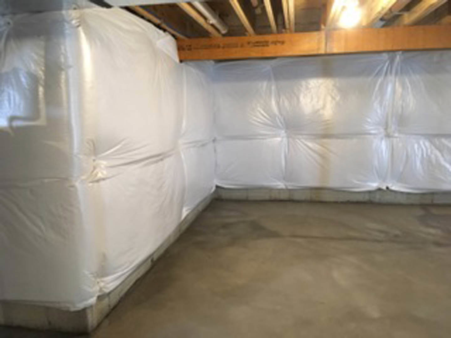 Room with white plastic coverings draped over furniture, concrete floor, and visible plaster walls and ceiling