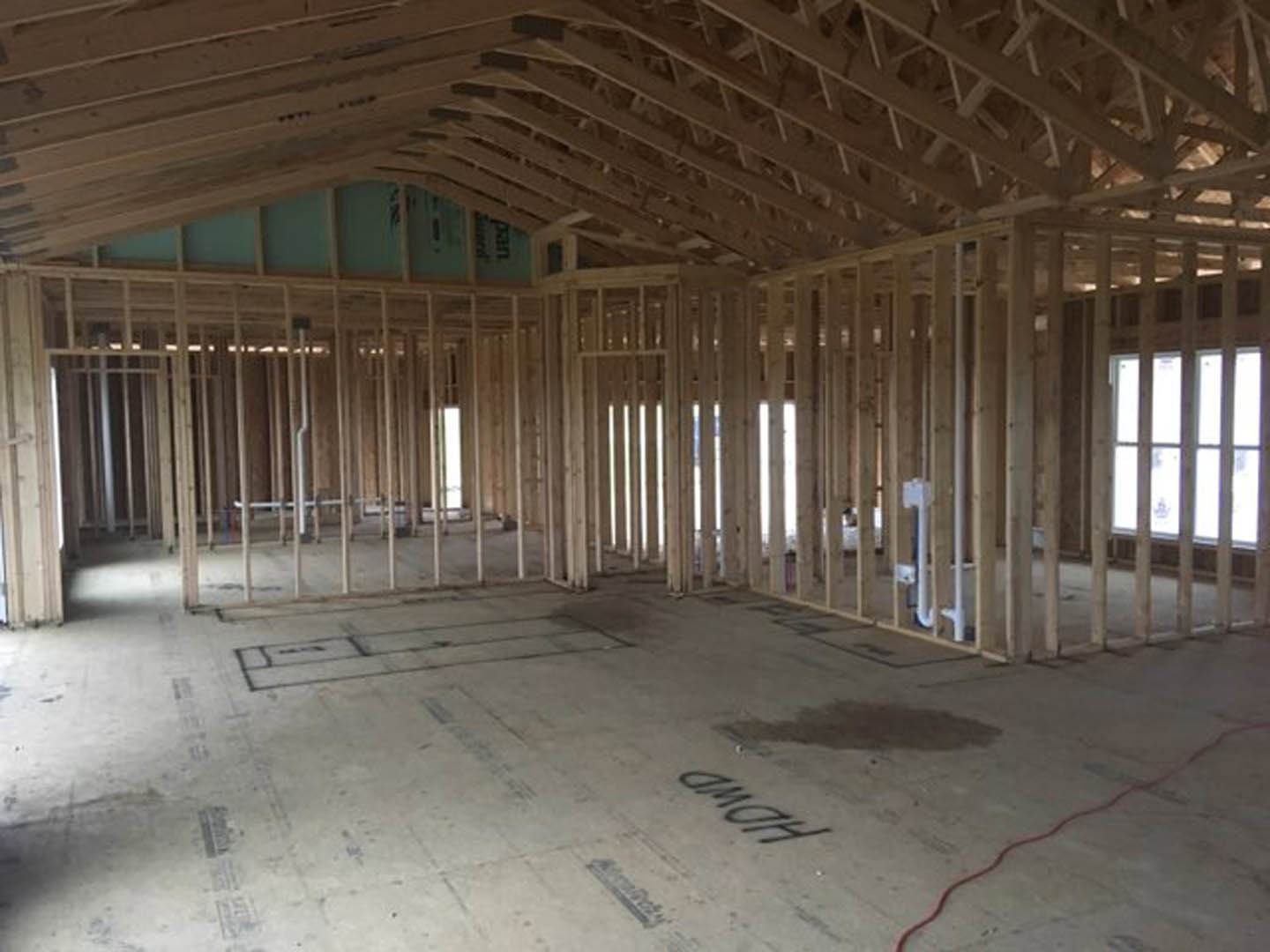 Open room with exposed wood ceiling beams, concrete floor featuring black text, large window allowing daylight, red cable lying on ground, unfinished surfaces.