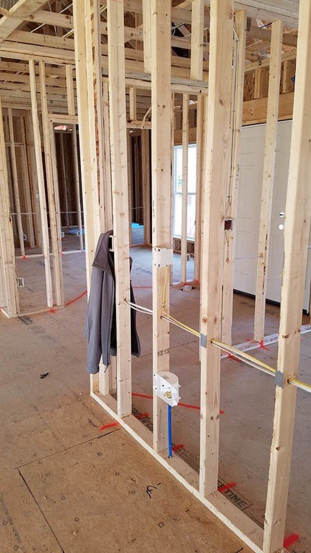 unfinished room with exposed wood framing, red tape on beams, white-framed window, partially installed door, and construction materials on floor