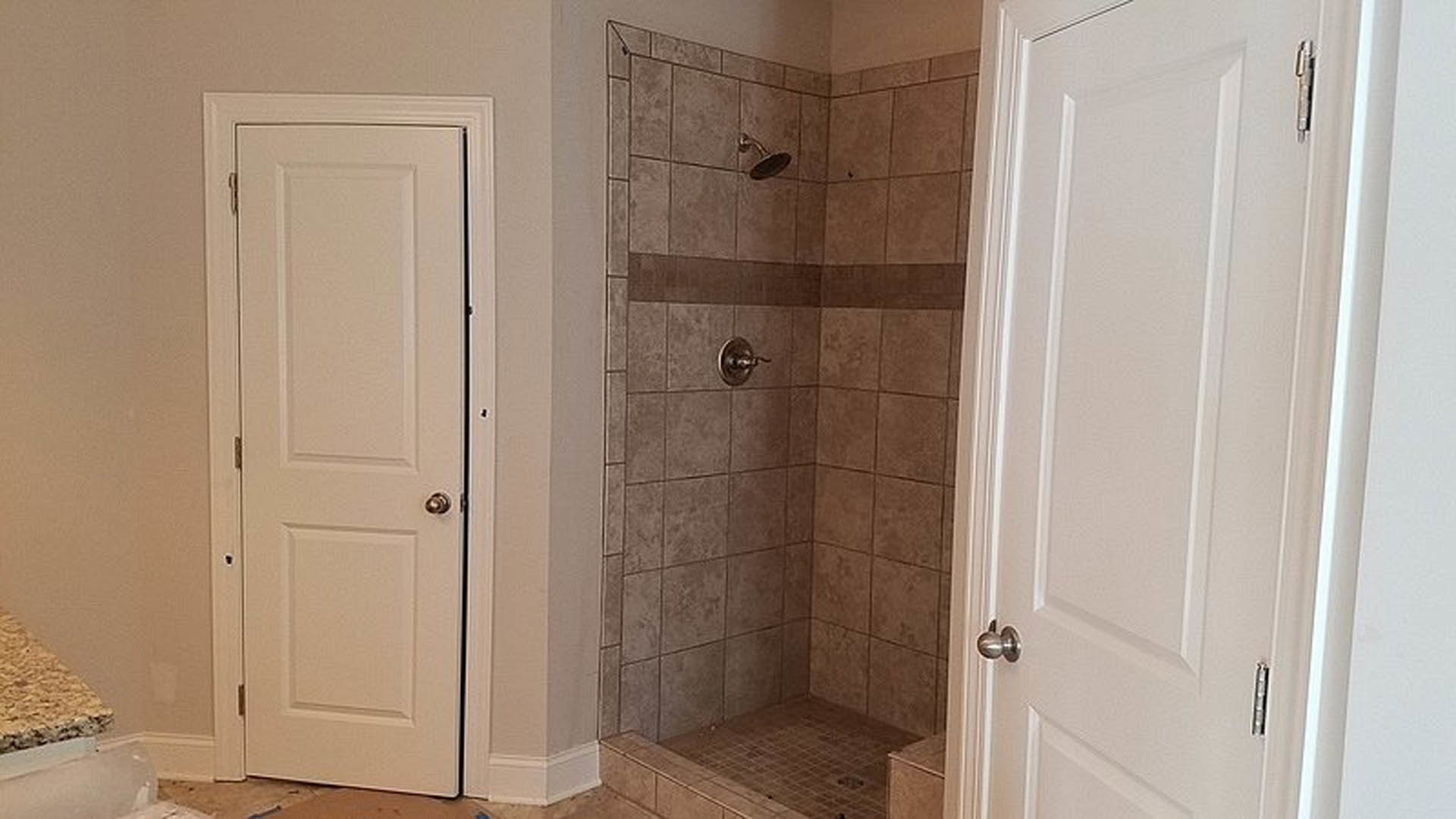 Walk-in shower with glass door, light gray tile walls, built-in niche, and adjacent white cabinetry in modern bathroom