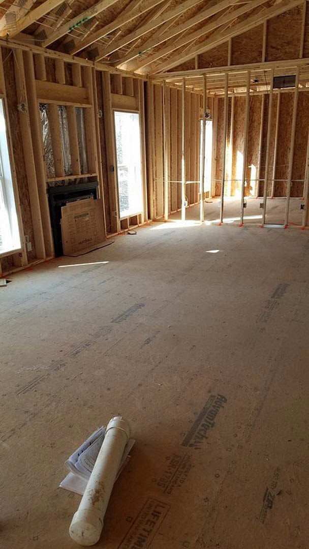 Living room with natural wood plank walls, exposed ceiling beams, stone fireplace, hardwood flooring, and large window letting in daylight