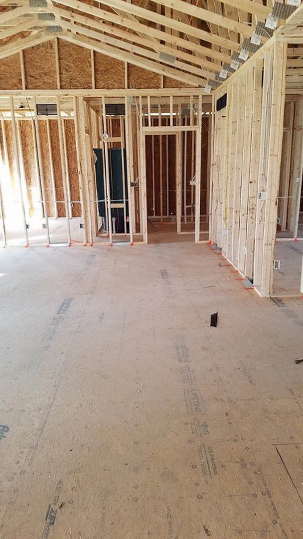 Wood-framed room under construction with exposed beams, ladder, unfinished flooring, and a close-up view of a window framed in lumber.