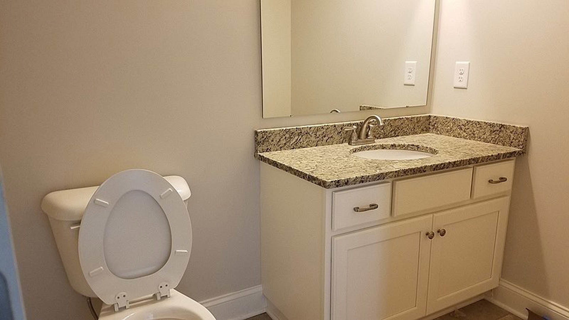 Bathroom with marble countertop vanity, undermount sink, white toilet with seat up, light tile flooring, and neutral wall tiles