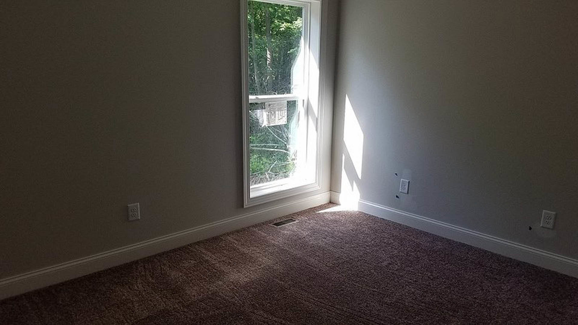 Large window set in a plaster wall, natural daylight streaming onto light wood flooring in a modern residential interior.