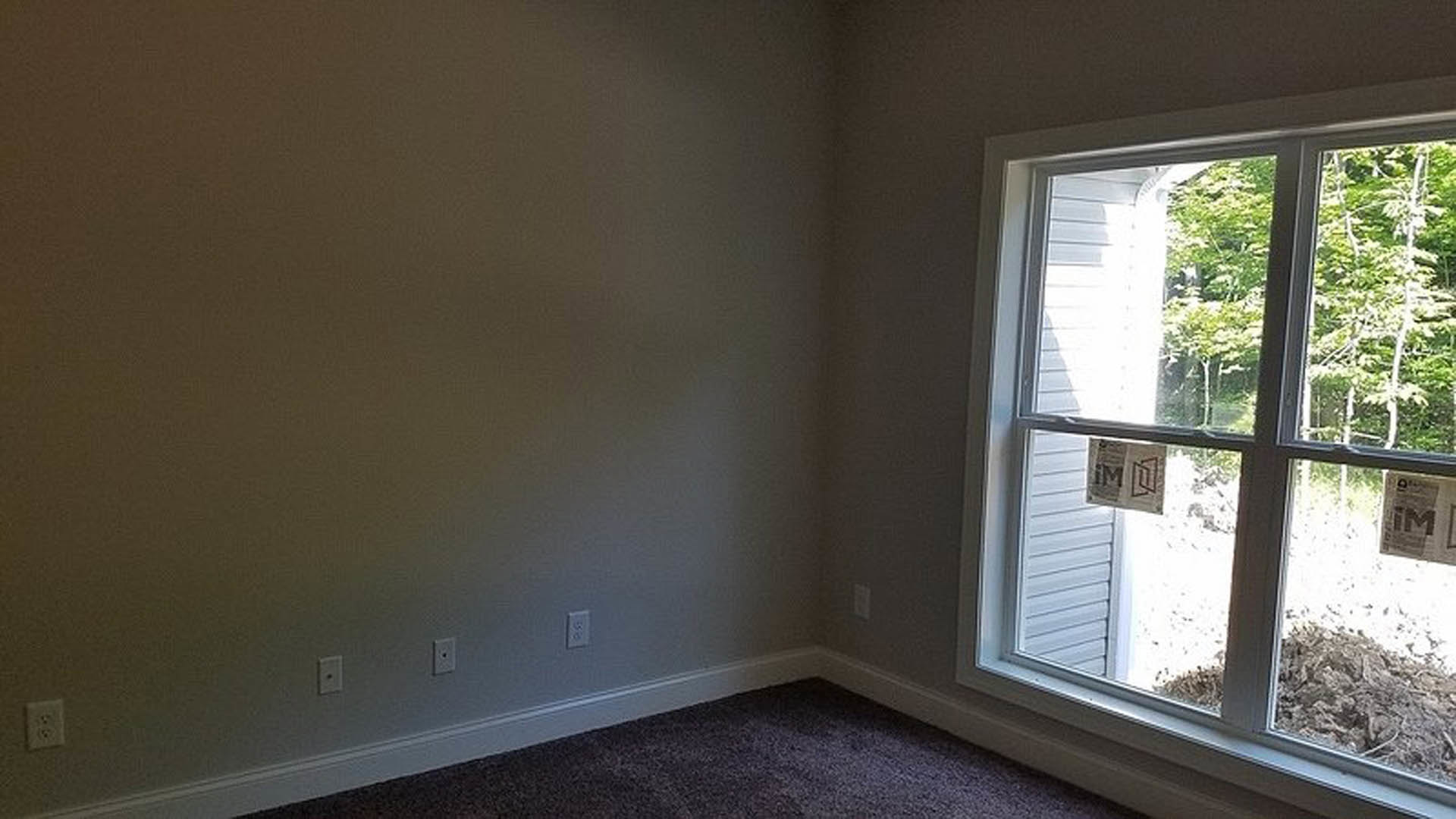 Large window with white blinds set in a neutral wall, electrical outlet below, natural daylight illuminating the interior space
