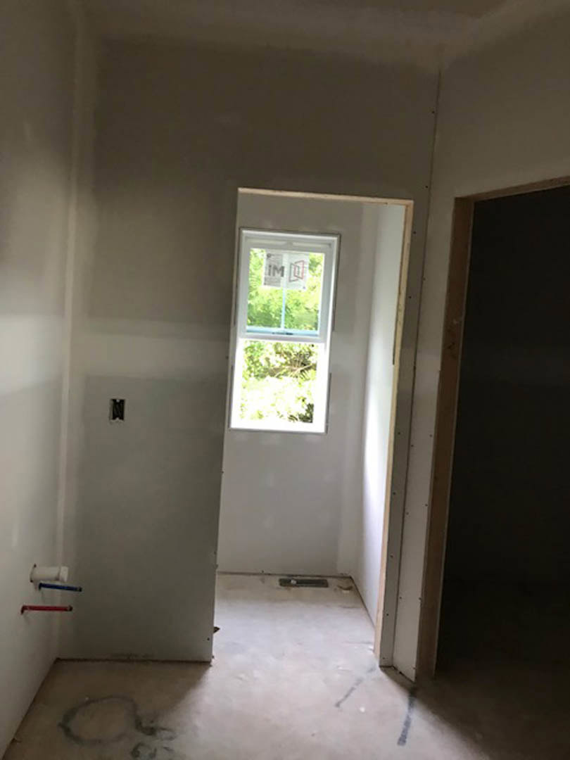 Modern interior room featuring a white plaster wall, large window with a sign, black accent wall with white trim, blue decorative object centered on another wall, light wood