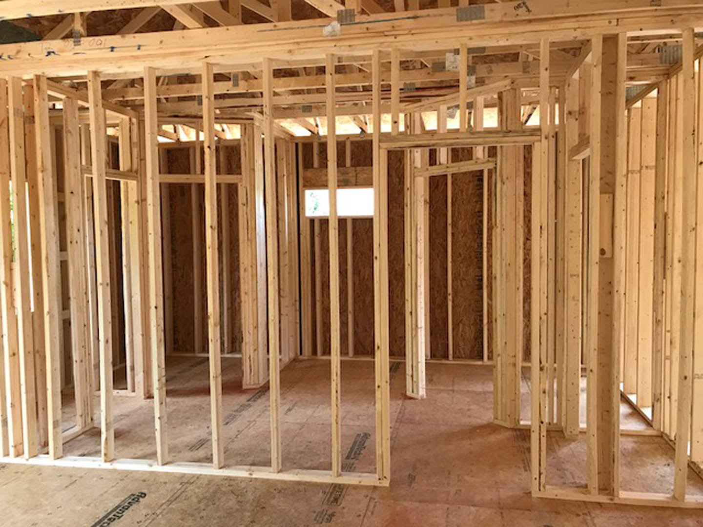 Exposed wooden framing and beams with unfinished lumber, construction materials, and a close-up view of a window opening in a residential home under construction