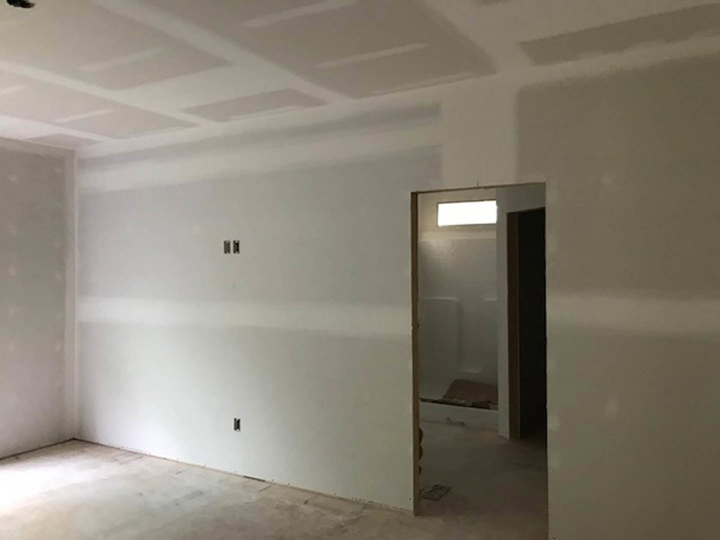 White bathroom with open door, smooth plaster walls, light-colored flooring, and ceiling fixture visible.