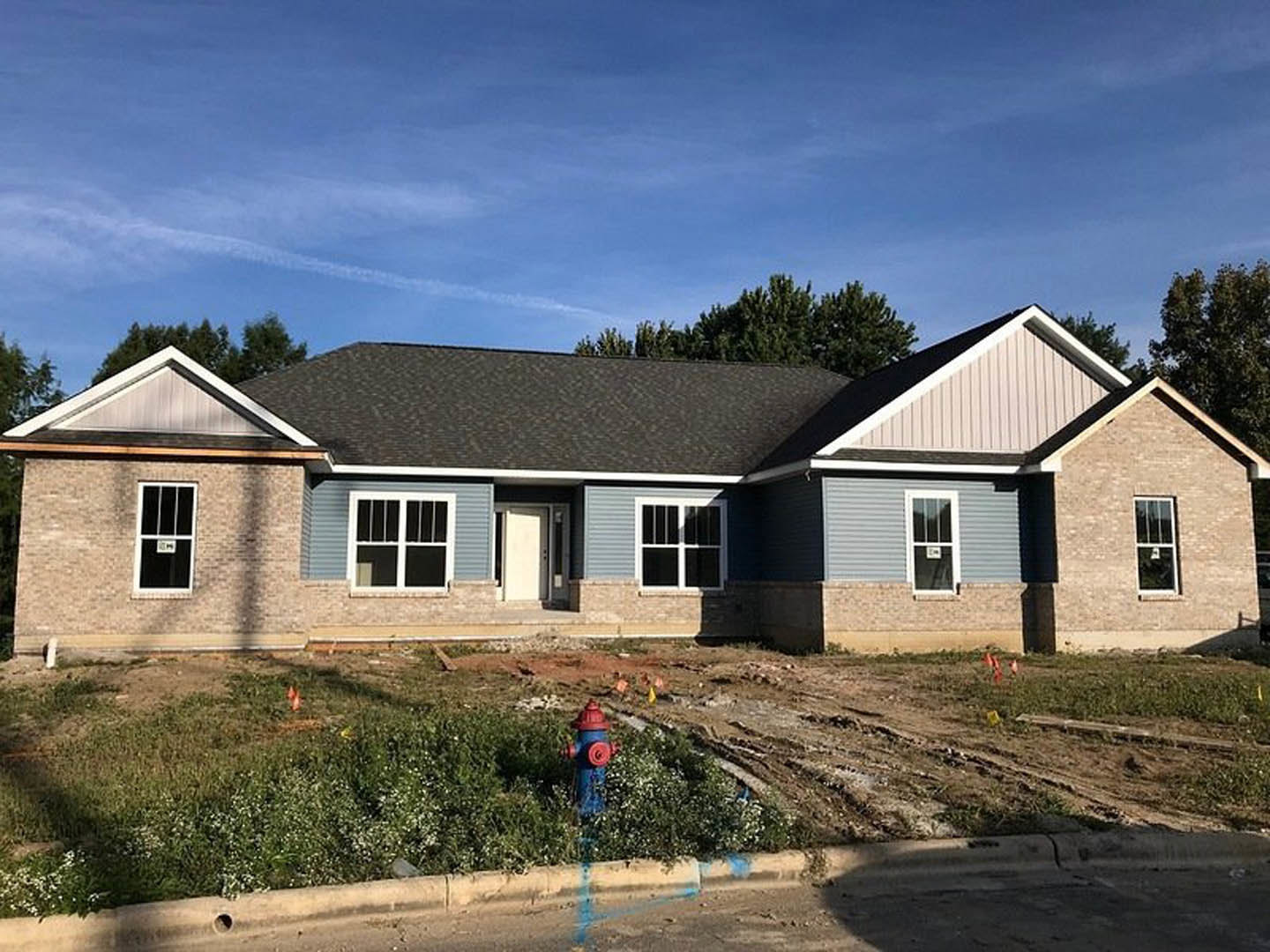 Partially built house with white framed windows, white door with black trim, fire hydrant in front yard, blue sky and clouds overhead