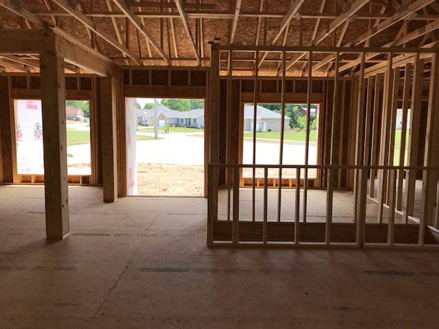 Unfinished room with exposed wooden ceiling beams, large window, and partially installed wooden floor, overlooking street through construction fencing