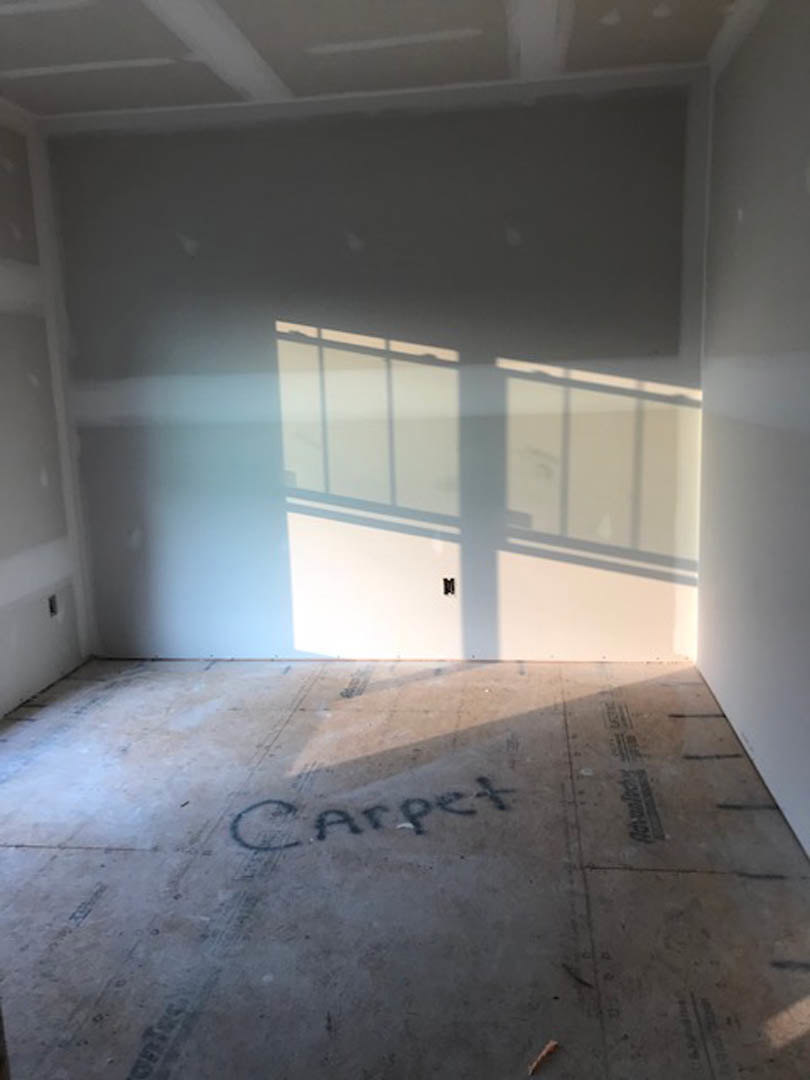 White plaster wall with black border, sunlight casting window shadow, light fixture illuminating wall, hardwood floor, ceiling detail visible.