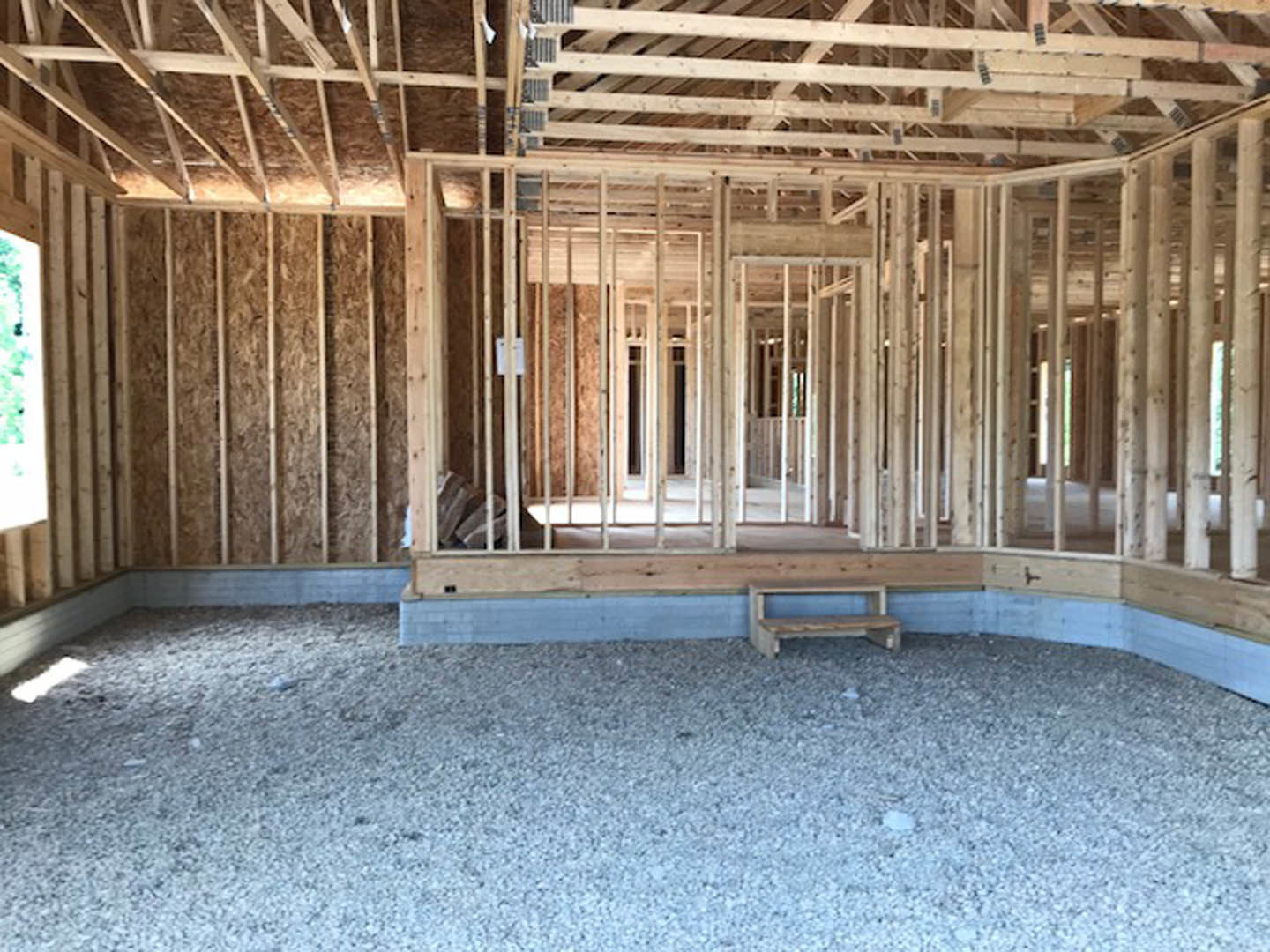 Wooden ceiling beams and unfinished walls in a residential interior under construction, gravel covering the floor.