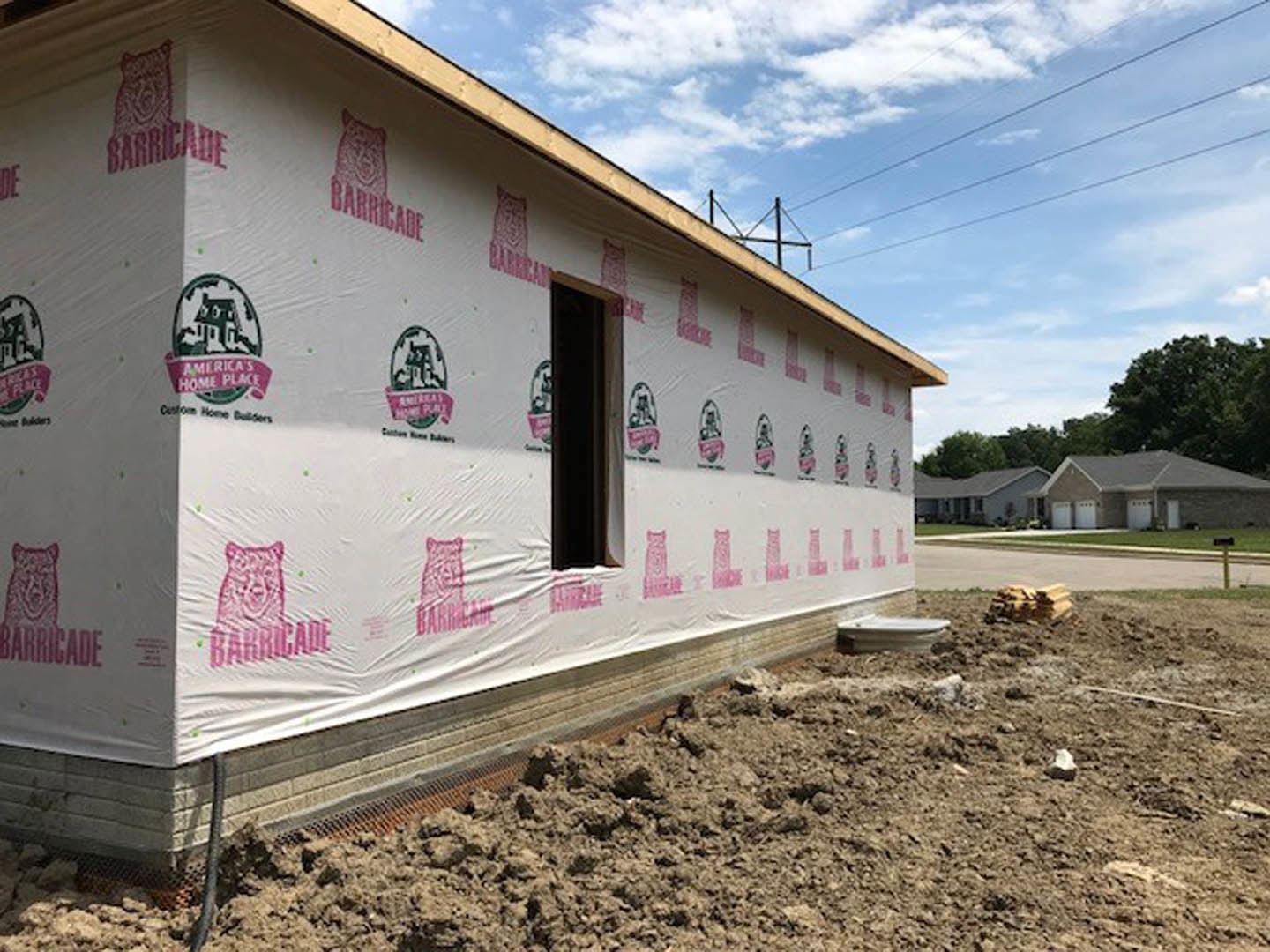 White exterior wall with pink logo, surrounded by trees and cloudy sky