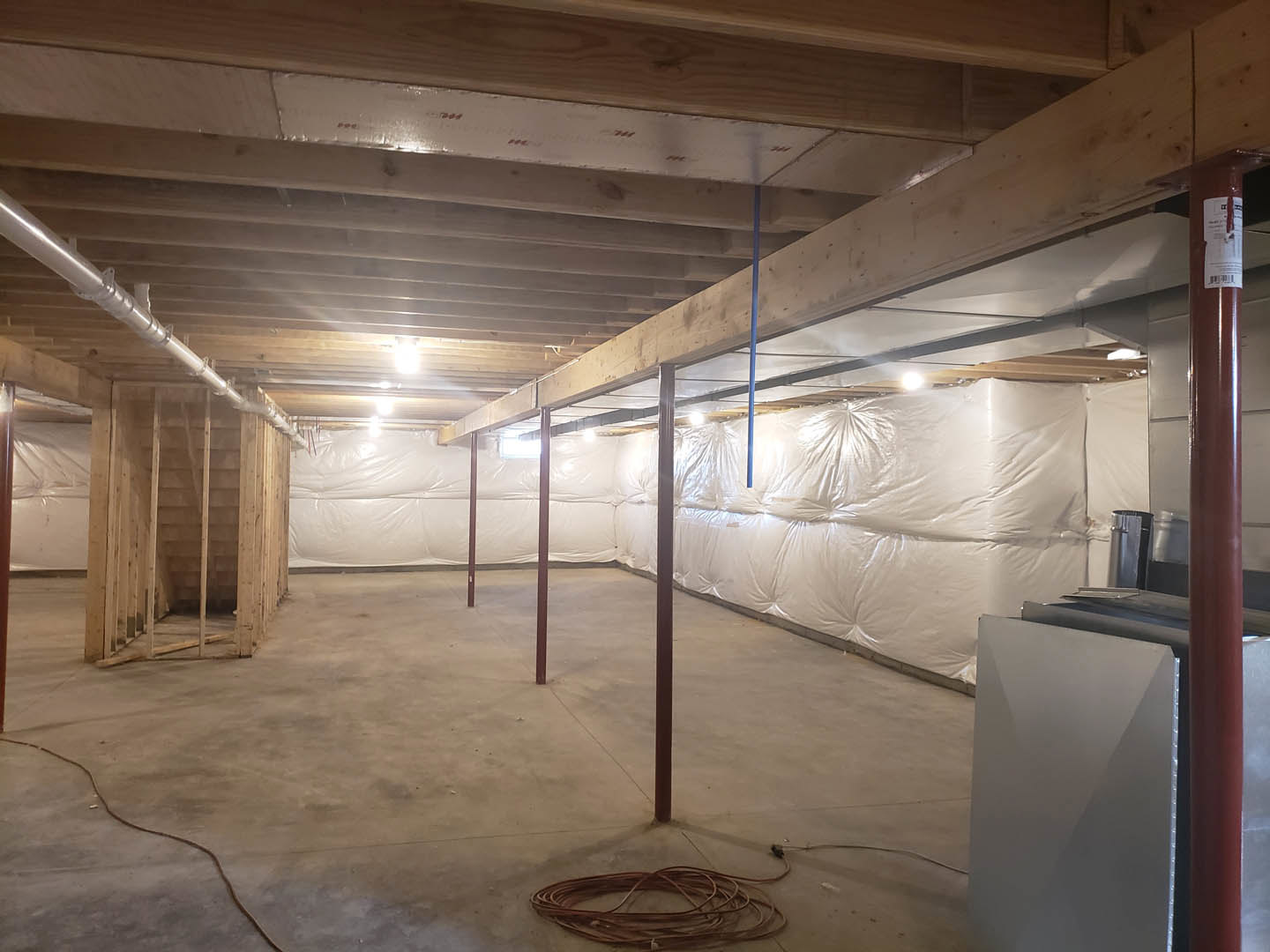 Unfinished room with exposed wooden beams, plaster walls, and a white sheet draped over the floor; visible staircase framing and construction materials scattered throughout.
