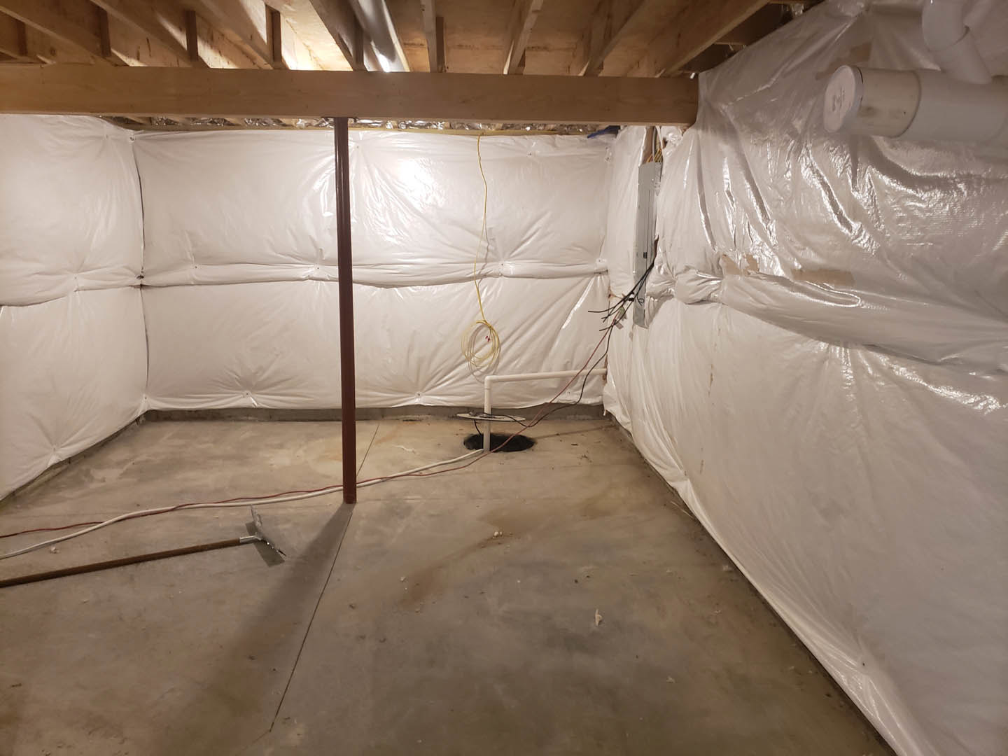 Unfinished room with white plaster walls, plastic coverings on the floor, exposed pipe, and construction tools scattered on concrete flooring
