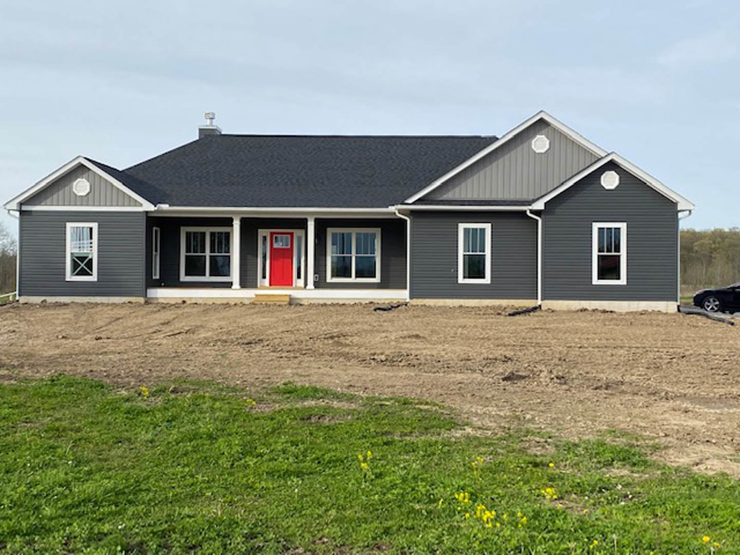 Two-story house with white siding, red front door, white-framed windows, and dirt yard under a partly cloudy sky