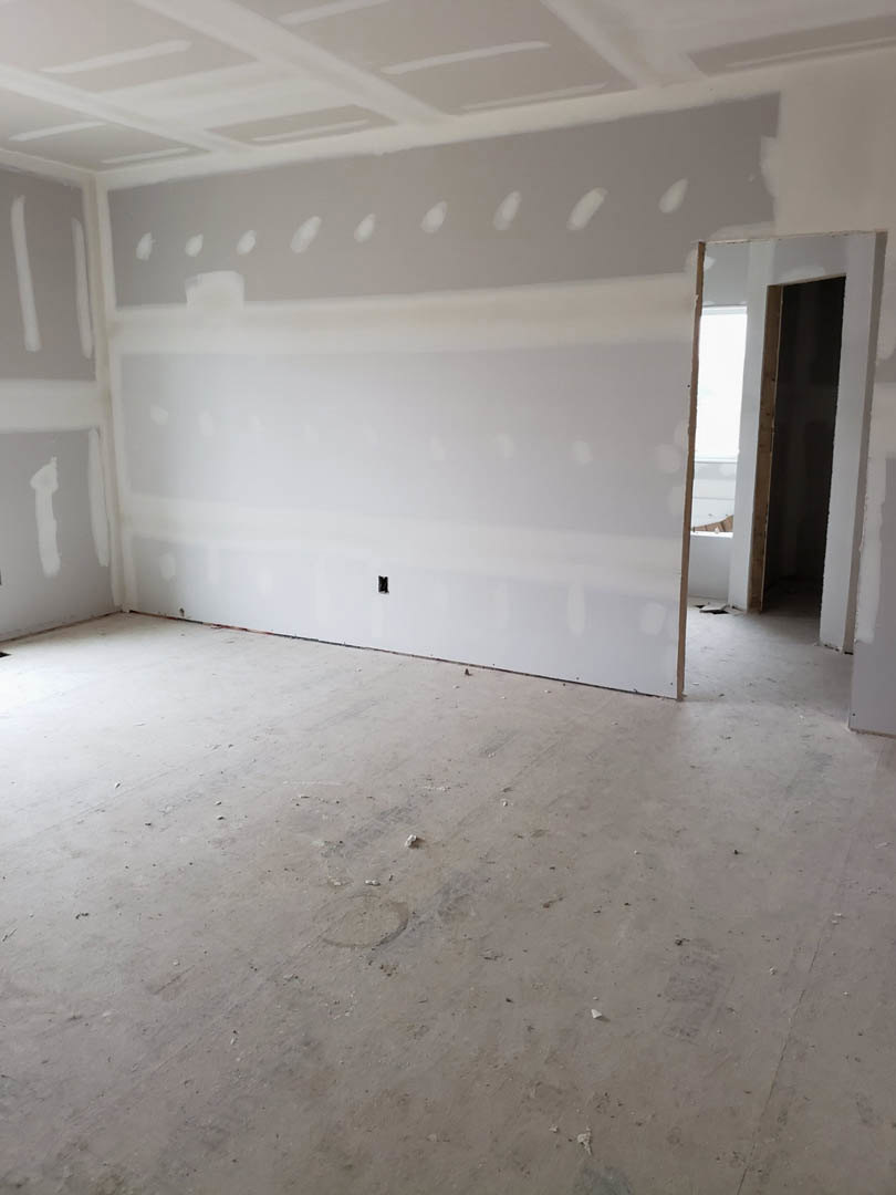 White-walled room with open door, unfinished concrete floor, hole cut into plaster wall, white ceiling with recessed light