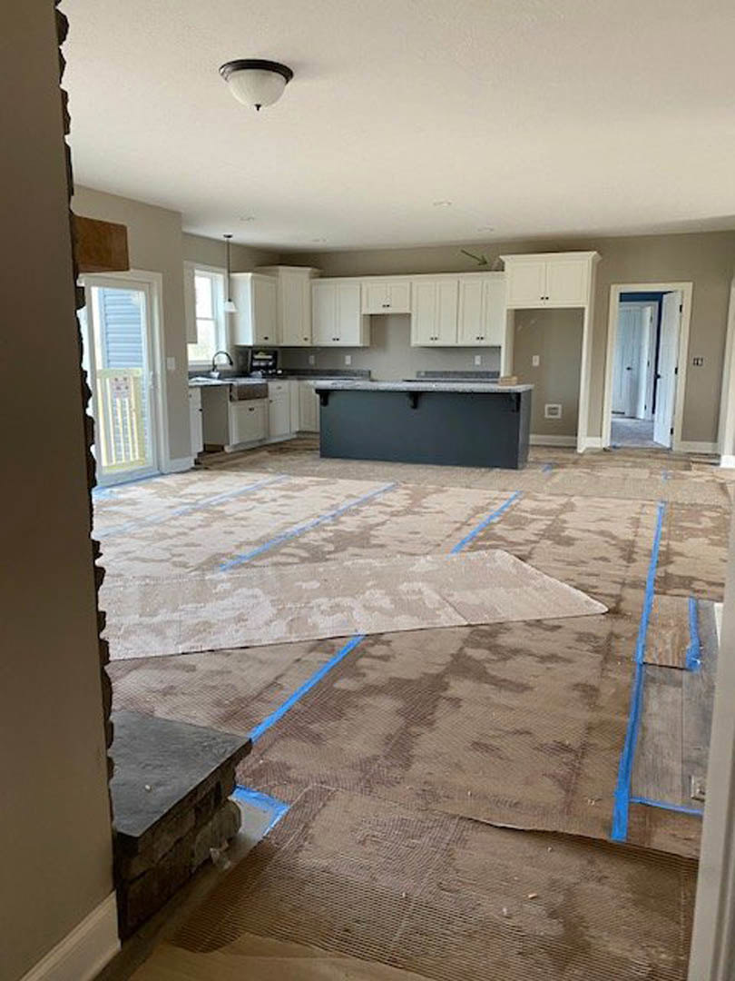 Modern kitchen featuring a stone bar counter, tile flooring, white chair near a window with blinds, plaster walls, and a carpeted area adjacent to a door.