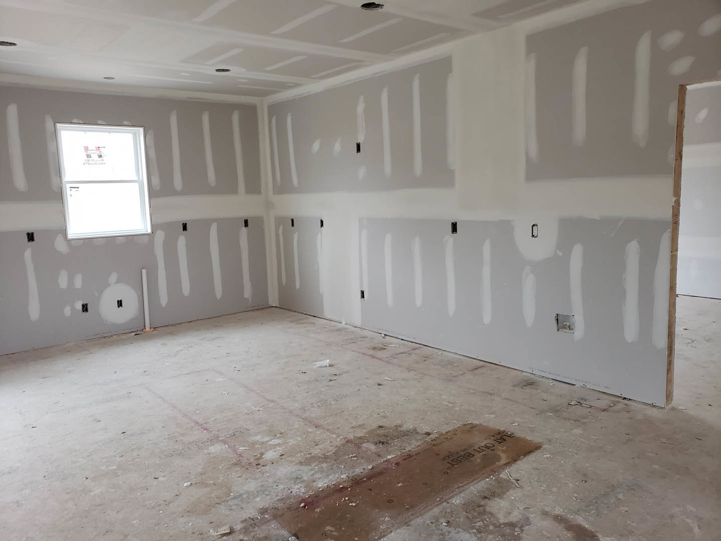 White-walled room featuring a rectangular window with white frame, white ceiling with recessed light, and a floor with visible dirt.