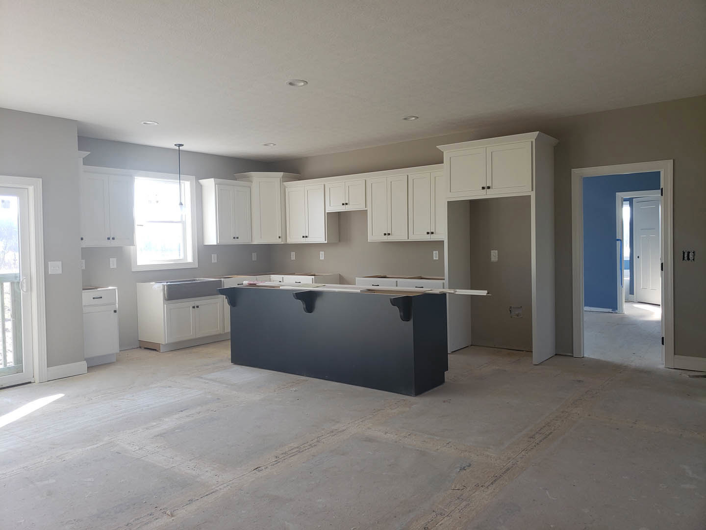 White kitchen cabinets paired with a black island, light tile flooring, stainless sink, and modern black hardware, with sunlight streaming through nearby windows.