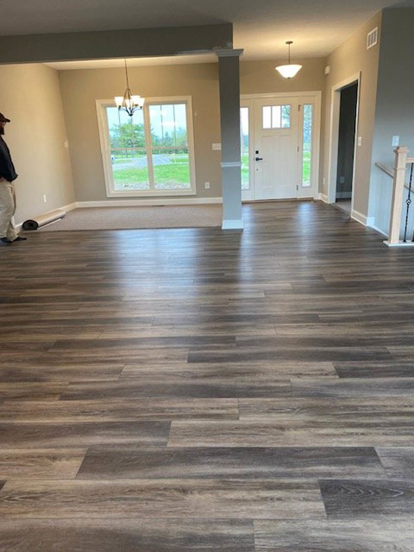 Man in black shirt standing on hardwood floor in bright room with white walls, ceiling light fixture, and white door featuring a window.