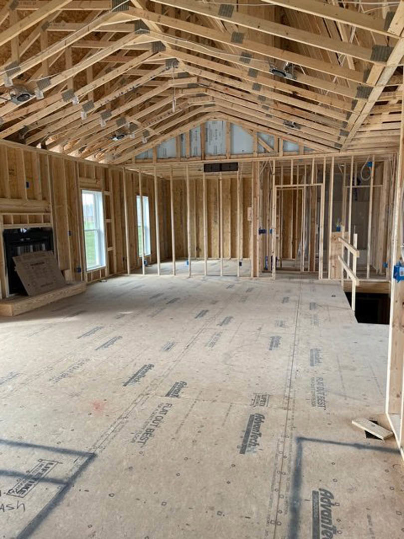 Unfinished room with exposed wood ceiling beams, concrete floor, window overlooking green grass, and construction materials on a shelf