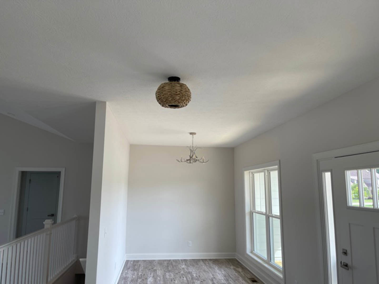 Chandelier and ceiling light fixture above grey carpeted floor, white railing, paneled door, and plaster walls with decorative molding