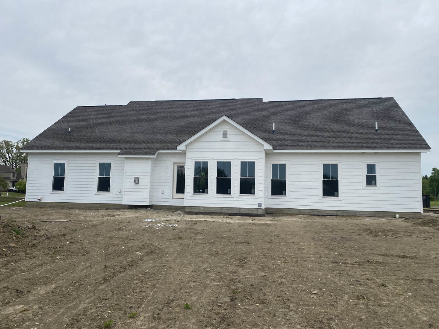White house with multiple windows and white trim, situated behind a large dirt field under a cloudy sky