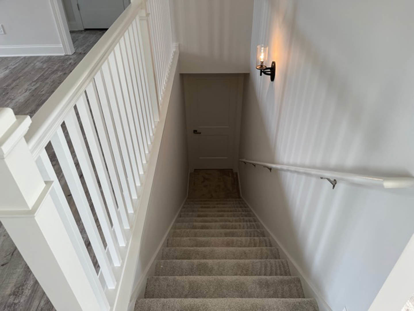 Carpeted staircase with white railing, black door handle, white walls, and modern light fixture