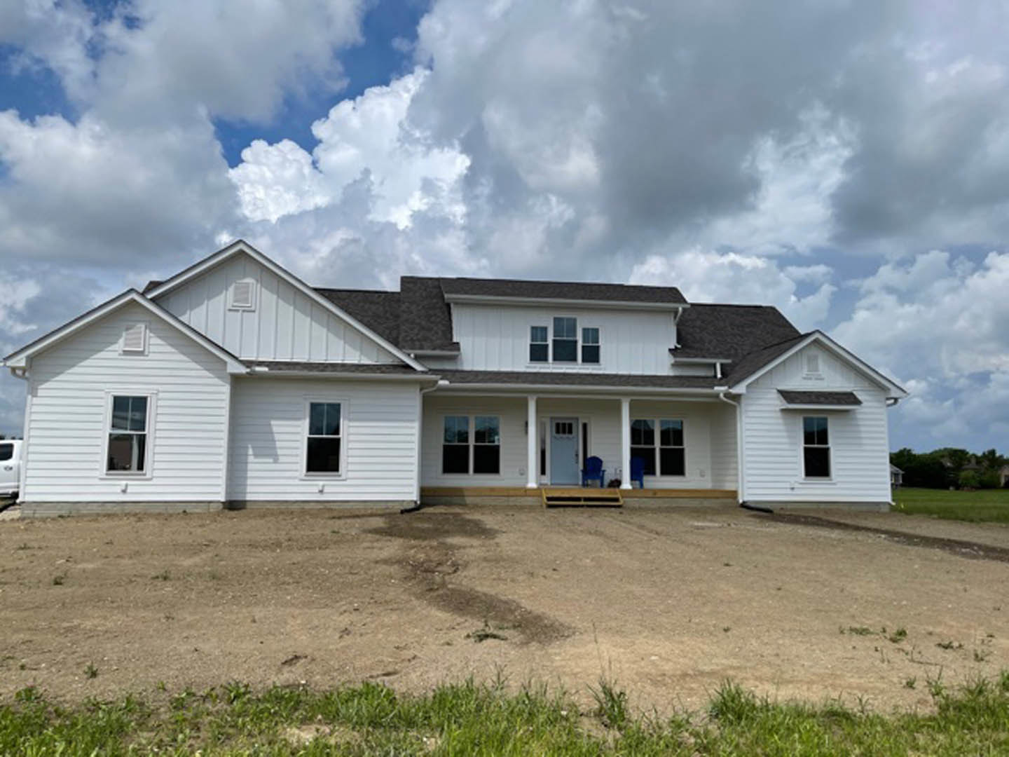 Two-story house with blue front door, white-framed windows, covered porch, and dirt yard under partly cloudy sky