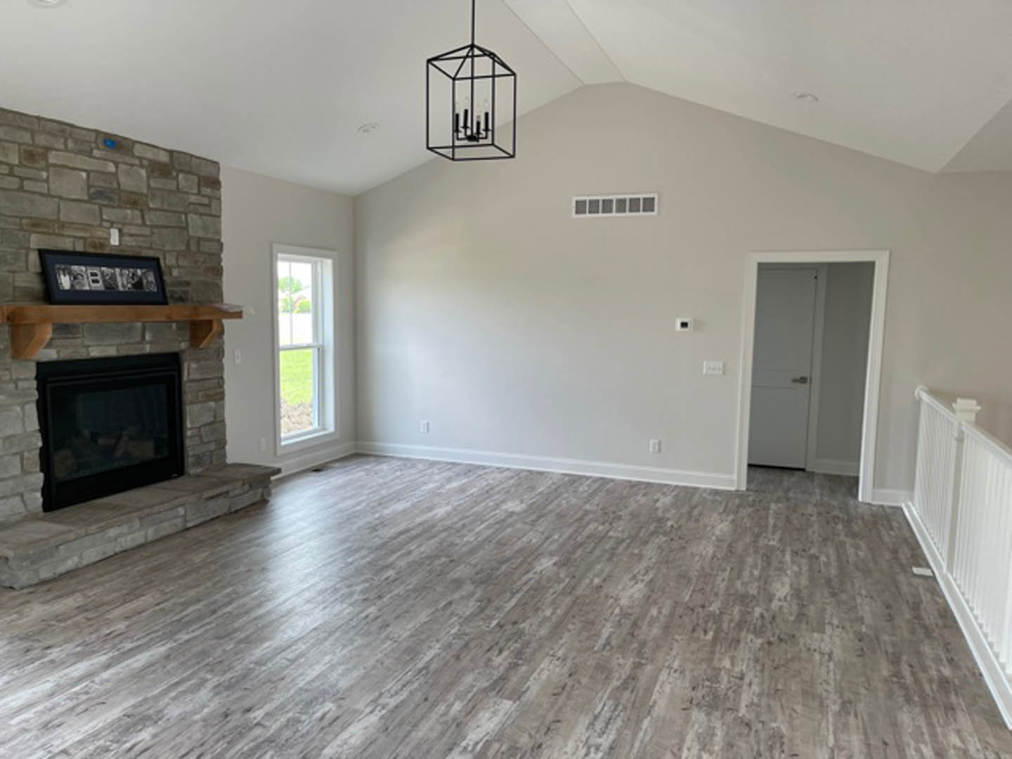 Living room with hardwood floors, white walls, glass-door fireplace, black metal candle holder, window overlooking green lawn, and white door with silver handle