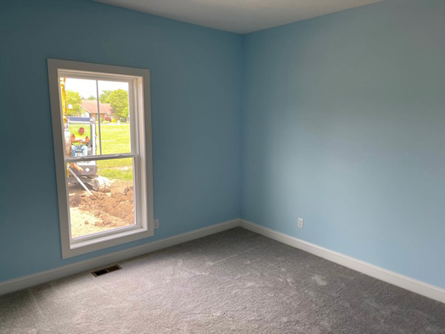 Blue accent wall with white-framed window overlooking construction site, carpeted floor, plaster finishes, natural daylight illuminating interior space