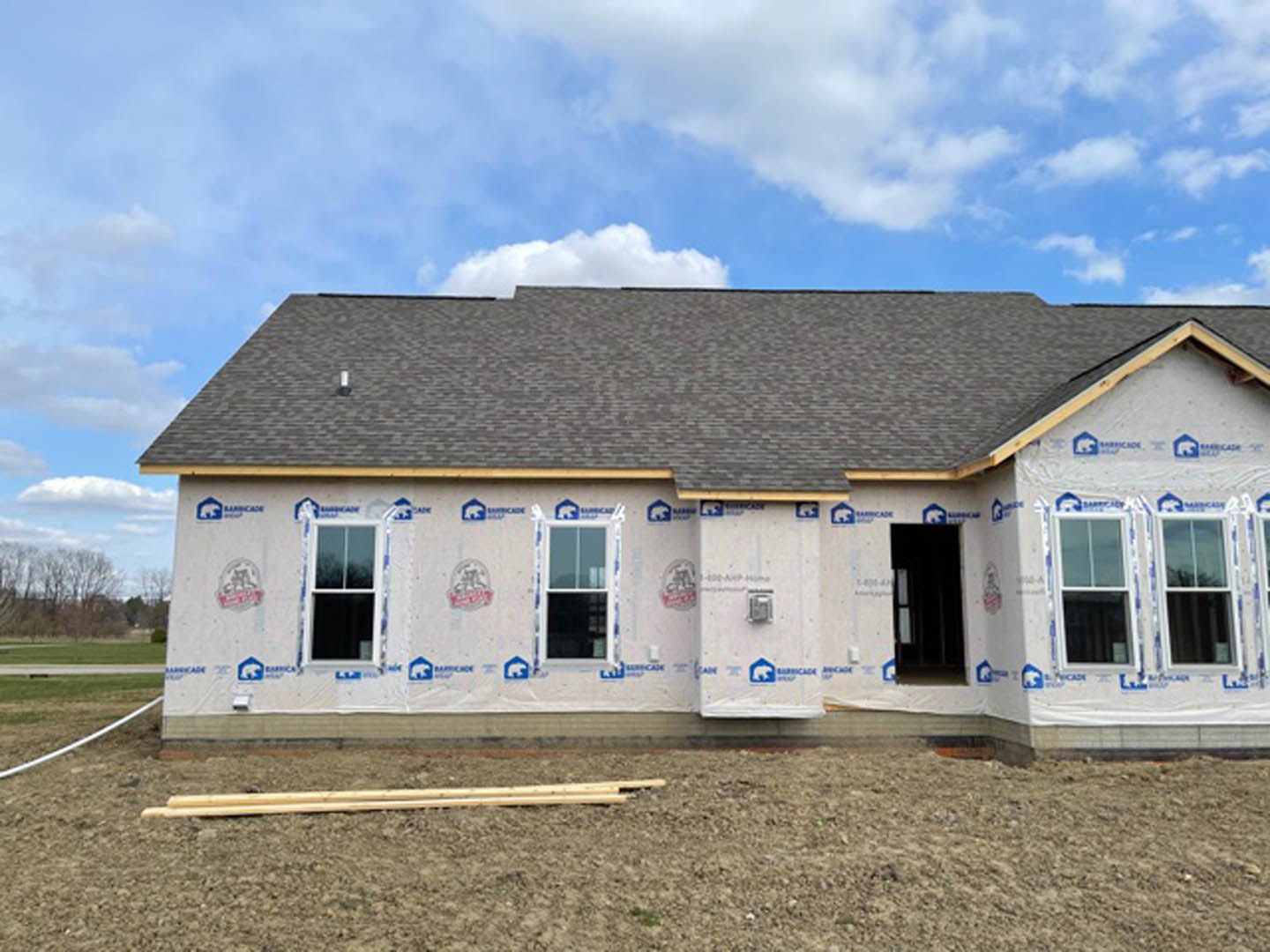 Framed house under construction with exposed insulation, white window frames, unfinished roof, and clear blue sky in background