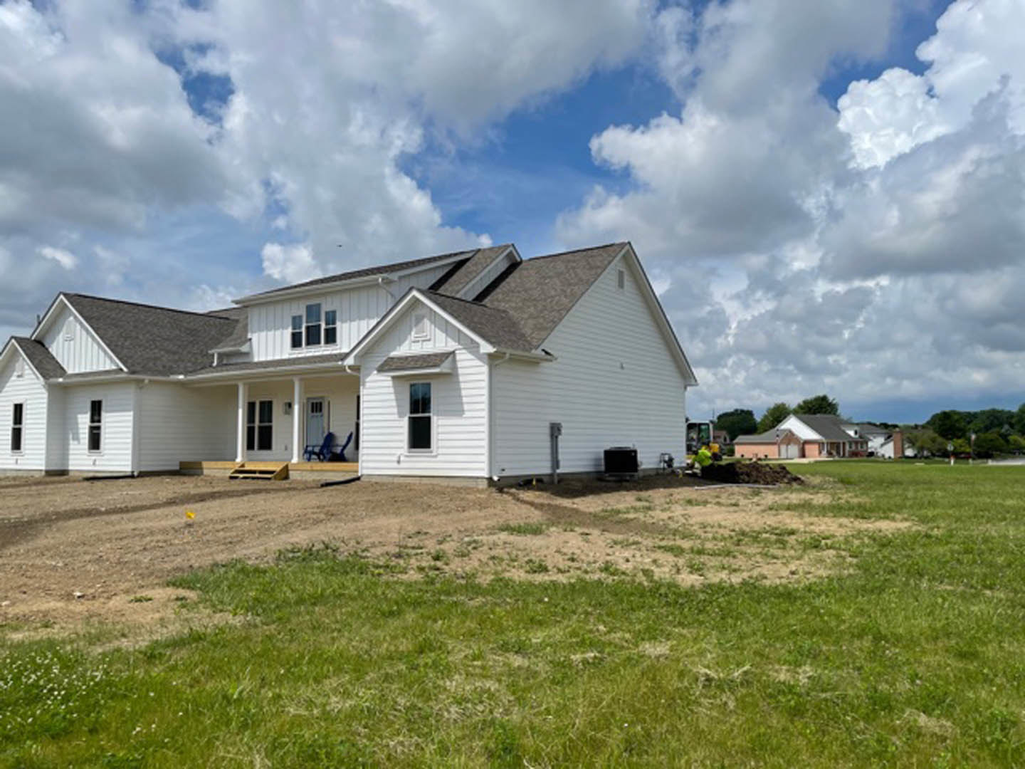 White siding house with large windows, blue chair on front porch, surrounded by green lawn under clear blue sky with scattered clouds